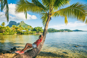 Tropical travel nature background tourist woman on eco tourism destination relaxing lying down on palm tree tropical landscape. Bora Bora island with Otemanu mountain view, Tahiti, French Polynesia.
