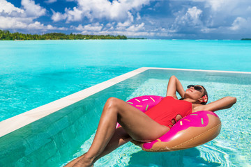 Summer swimming pool woman relaxing on donut float enjoying luxury resort vacation sunbathing fun....