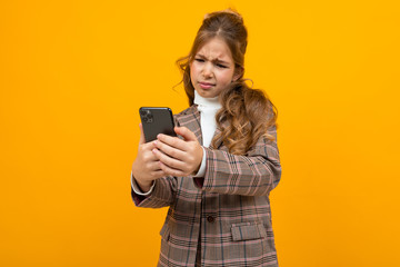 Naklejka premium cute caucasian blond girl in a classic jacket makes selfie on the phone in the studio with a yellow background
