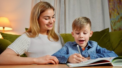 Beautiful mother and son studying together at home. Home education concept. Nanny teaching a boy at home doing homework.