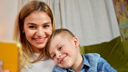 Beautiful mom and son making selfie at home. Happy family having a facetime video call. Unity, connection, technology concept