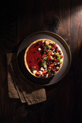 Food styling with fresh fruit tart berries. Flat lay of the open pie with strawberries, raspberries, blueberries, cranberries and mint leaves. Shot in a dark key on a wooden background.