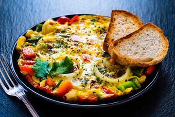 Breakfast - scrambled eggs with vegetables on black stone background