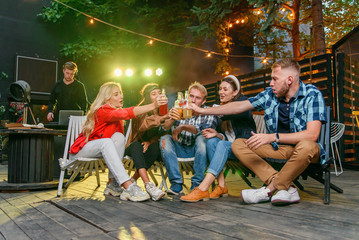 Fototapeta premium Friends clinking bottles and drink beer at outdoors cozy party with music and colored disco lights.