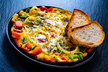 Breakfast - scrambled eggs with vegetables on black stone background