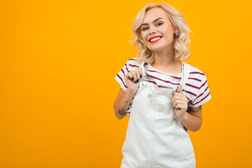 Beautiful young woman with short blonde curly hair and bright makeup in white overalls gesticulated...