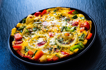 Breakfast - scrambled eggs with vegetables on black stone background