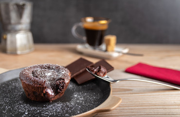 Warm chocolate lava cake on a black plate with a cup of coffee on a dark background