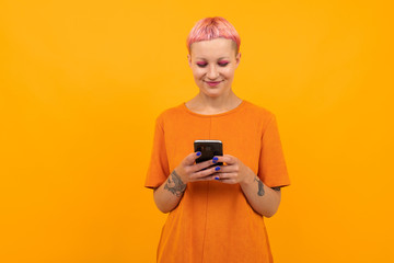 Fototapeta premium Extraordinary beautiful woman with short pink hair and big tattoo on her hand smiles isolated on orange background