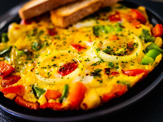 Breakfast - scrambled eggs with vegetables on black stone background
