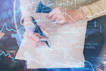 Hand taking notes in notepad. Forex chart holograms in front. Concept of research. Multi exposure