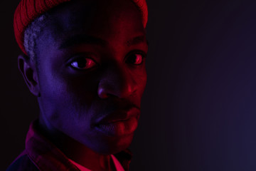Closeup portrait of a stylish handsome black man looking at the camera in neon light in the shade
