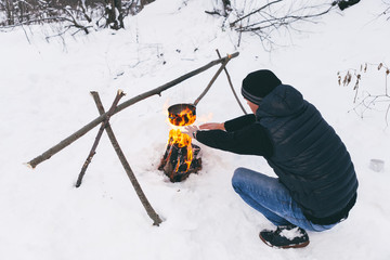 Man is preparing a fire and boiling water for cooking, winter camping.