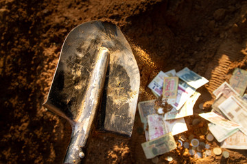 Burying money in the sand. Fill coins and bills with earth with a shovel.