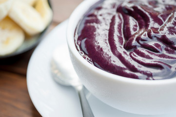 Fresh bowl of purple Amazonian acai in a clean white bowl with a side of banana slices on wooden table in Brazil