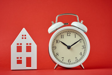 White retro alarm clock and miniature house on the red backgroumd