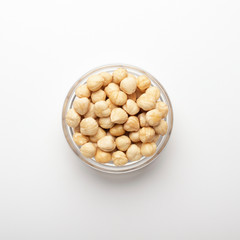 Pile of hazelnuts in glass bowl on white background