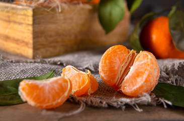 slices of juicy peeled tangerine on a napkin on a wooden background, a whole tangerine with leaves in the background