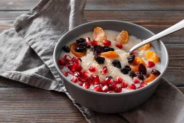 plate of oatmeal porridge with Mandarin slices, pomegranate seeds, raisins, dried apricots on a gray napkin on a wooden background
