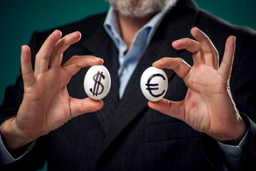 A portrait of man in suit holding white eggs with drawing dollar  and euro sign. Business and finance concept