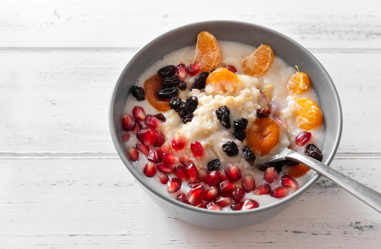 plate of oatmeal with fruit, porridge, dried apricots, raisins, pomegranates, Mandarin slices on a white background, healthy Breakfast