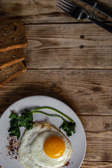 Eggs with seasonings and greens on a white plate with cutlery and rye bread on a wooden table