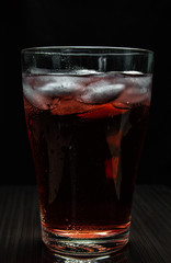 Glass of cherry juice with ice cubes on black background