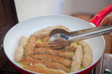 The long cutlet is fried in a red pan. She cooks the cutlet in a white pan.