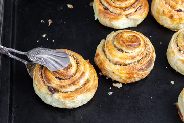 sweet croissant brioche snail with raisin-walnut filling with confectionery tongs on black baking tray