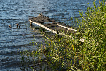Remnants of the old abandoned wooden bridge. Desolate pier. Forest and sky reflection on water. Shore of a single lake