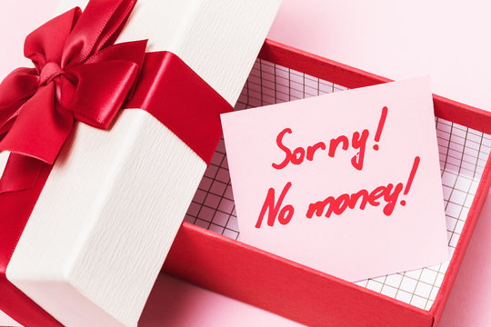 An open gift box with a note inside on a pink background. Concept on the topic of lack of money for gifts
