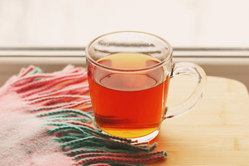 Glass transparent Cup of black hot tea on a wooden table, next to a beautiful scarf of green and pink color with fringe. Selective focus. Relaxation over a Cup of tea