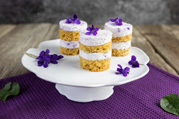 focus on violet flower small cakes with mascarpone violaceous cream on ceramic whatnot