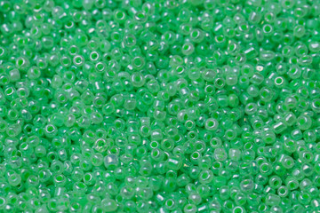 A large number of beautiful green beads in an even layer. Materials for needlework and creativity. Macro photography of objects. Background and texture for design.