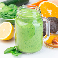 Green detox smoothie with avocado, spinach, cucumber, orange, lemon and honey, in a glass mason jar, square