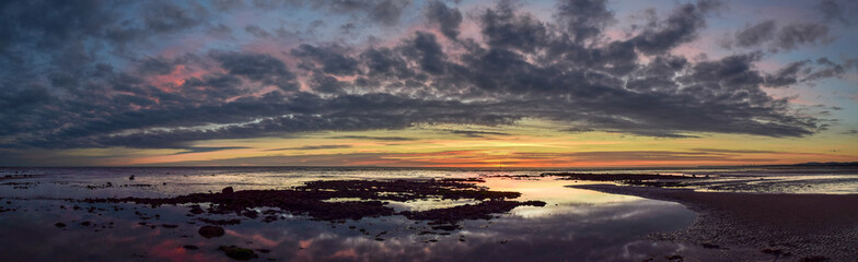 A colourful sunset reflected in rock pools and an Island on the horizon