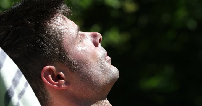 Man sunbathing outdoors in sunlight. Handsome man in 30s tanning face close-up