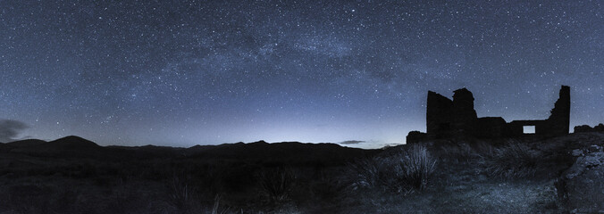 Milky Way arching of an derilict building high above a valley