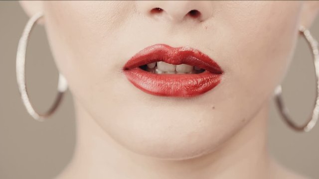 Close up red lipstick and red nails. Finger at the mouth. Perfect skin. Concept lip gloss. Decorative cosmetics. Secrets. Silence.