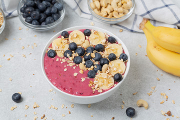 Healthy breakfast bowl: berry smoothie with banana, blueberries, granola and cashew. Summer dessert
