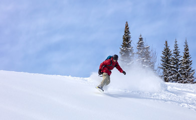 heliski snowboarding. freerider in a bright suit rides snowboarding with large splashes of snow on a sunny day. Young snowboarder. concept snowboard. big swirls of fresh snow in Good powder day