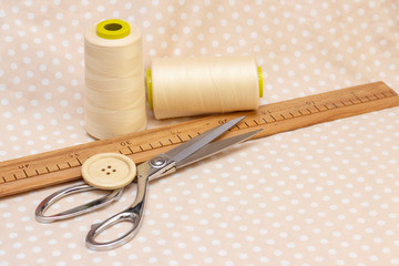 spools of beige cotton. scissors and a wooden button on a beige polka dot fabric. natural sewing concept