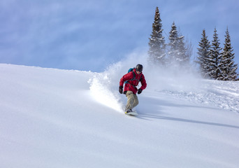 heliski snowboarding. freerider in a bright suit rides snowboarding with large splashes of snow on a sunny day. Young snowboarder. concept snowboard. big swirls of fresh snow in Good powder day