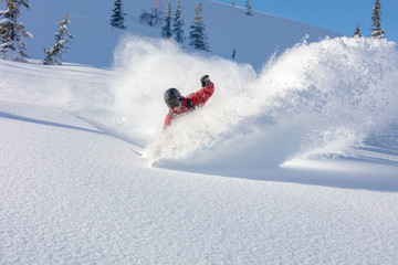 heliski snowboarding. freerider in a bright suit rides snowboarding with large splashes of snow on...