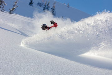 heliski snowboarding. freerider in a bright suit rides snowboarding with large splashes of snow on...