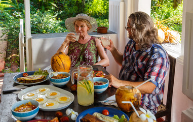 Mature couple has Breakfast with happy faces in an authentic setting, on the terrace of an ancient Villa on tropical island. Healthy food, fruits and vegetables on a wooden table .