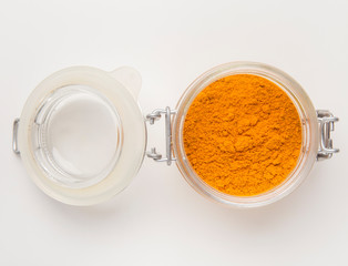 A glass jar filled with turmeric powder on white table