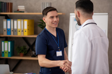 Young male intern looking cheerful while meeting chief doctor