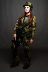 A girl soldier in camouflage clothing poses in a Studio