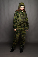 A girl soldier in camouflage clothing poses in a Studio